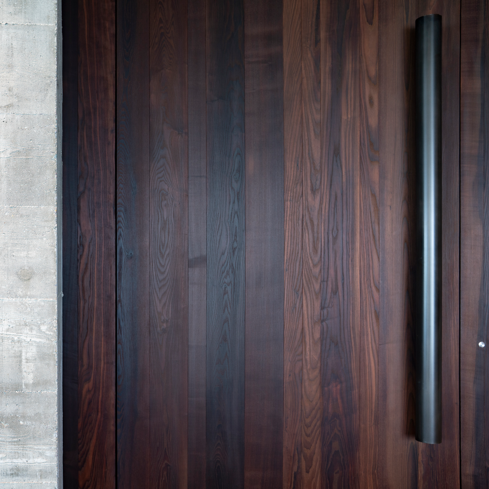 Oversized hand-crafted white oak and iron front pivot door with bronze hardware